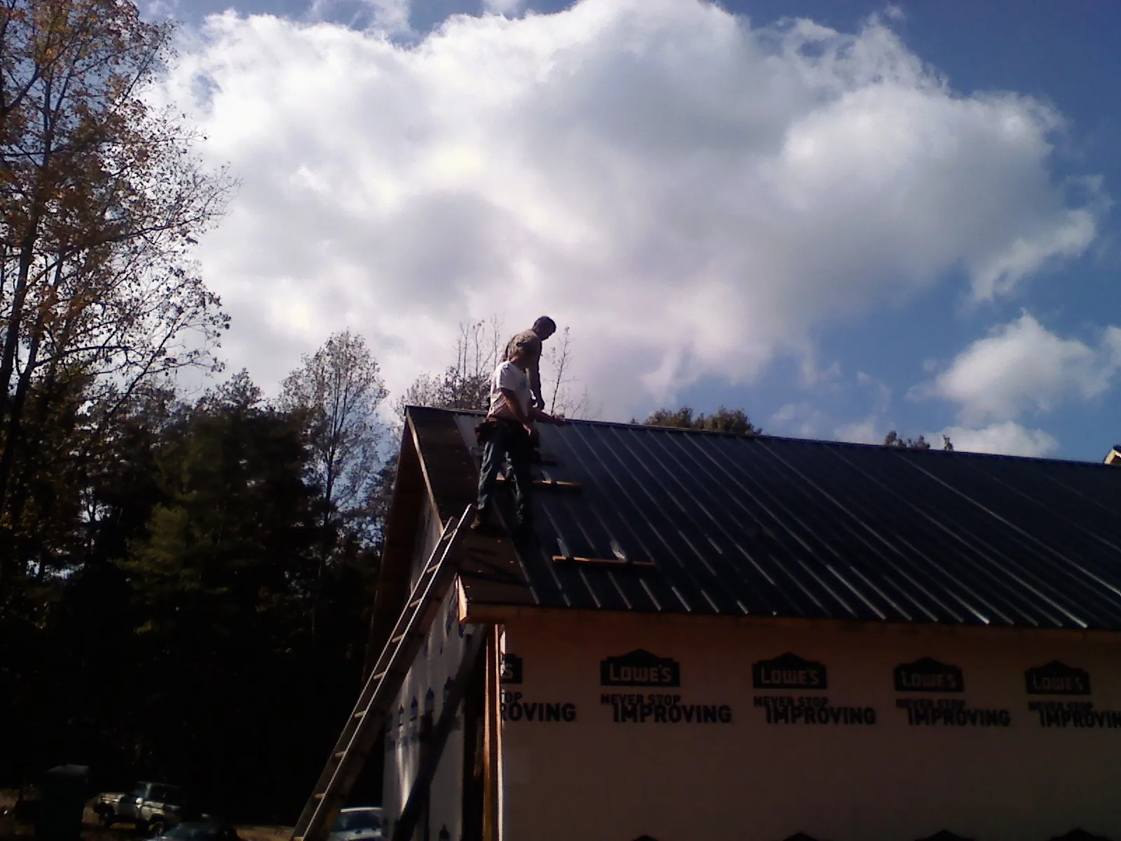 Roofer fastening dark metal panels high against a cloudy sky, from a Roof Inspection job in Plano